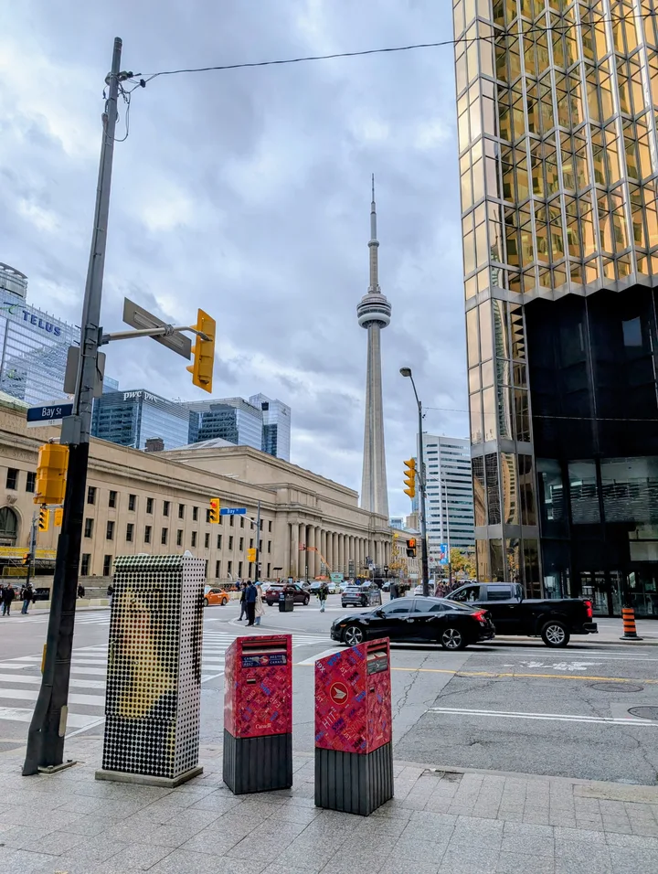 The CN Tower behind Union Station, framed by downtown buildings and a Bay Street intersection in Toronto.